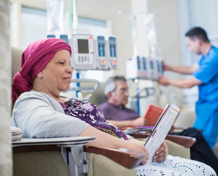 Woman reading a magazine while getting chemo infusions in a treatment center.